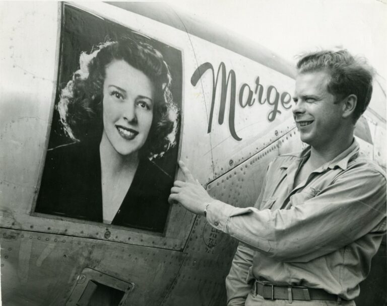black and white photo of man pointing to imprint of smiling woman's face on aircraft.